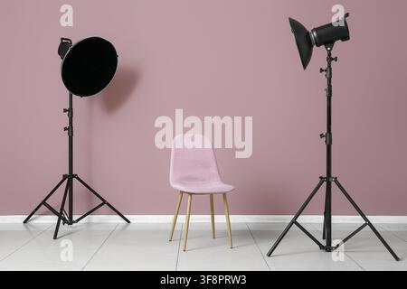 Empty pink chair with two studio lights on tripods against a mauve wall in a photography studio, Clean mauve wall background and a tiled floor, provid Stock Photo