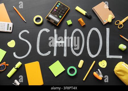 School supplies and stationery items arranged around the word "school" written in chalk on a blackboard, education Stock Photo