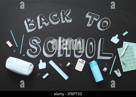 Back to school chalk text on a blackboard with various light blue and white stationery items, education Stock Photo