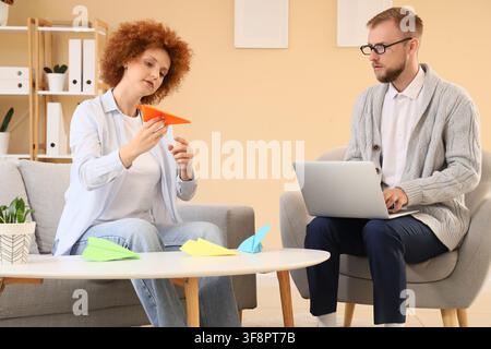 Woman holding an orange paper airplane while a man works on a laptop, creativity and innovation concept, the scene suggests a modern work environment Stock Photo