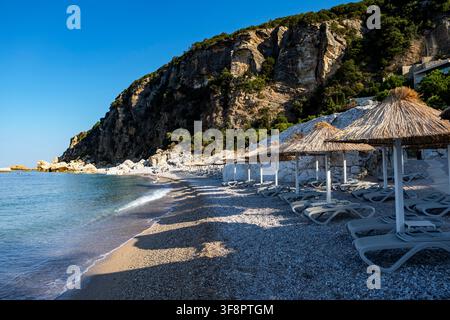 a tranquil beach scene featuring rocky cliffs and white umbrellas, set against a backdrop of a calm coastal landscape, evoking a sense of relaxation a Stock Photo