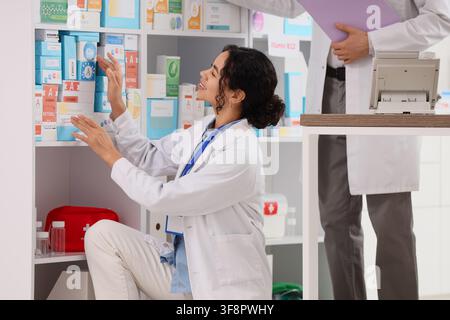 Female pharmacist organizing medicine boxes on shelves in a modern pharmacy healthcare and pharmaceutical industry Stock Photo