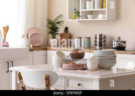Clean kitchen interior with white dining table, stacked dishes, and modern kitchenware for home living and organization Stock Photo