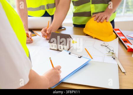 Architects and engineers reviewing blueprints with a house model and safety gear on a wooden desk Stock Photo