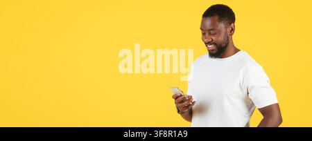 Happy Black Man Using Smartphone, Yellow Background, Technology Concept Stock Photo