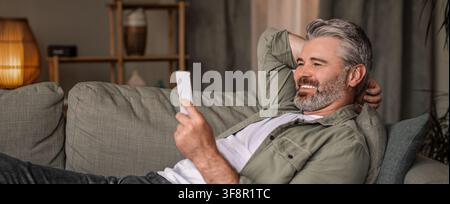 Happy Elderly Caucasian Man Using Smartphone Relaxing At Home, Lifestyle Concept Stock Photo