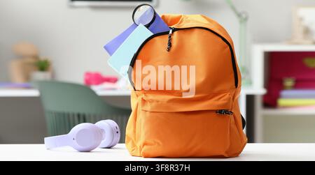 Orange backpack with school supplies and Purple headphones on a white desk, back to school Stock Photo