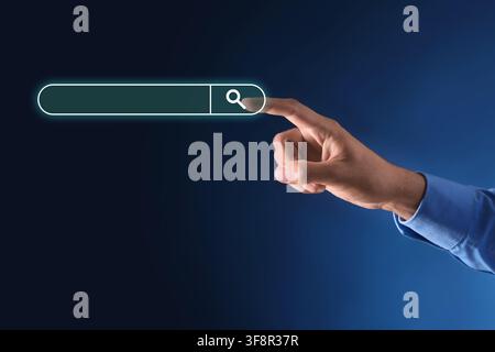 Human hand in blue shirt sleeve touching a glowing search bar with a magnifying glass icon on a dark blue background, the finger touches the magnifyin Stock Photo