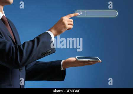 Businessman pointing at a glowing search bar with a tablet in hand, digital marketing and online information Stock Photo