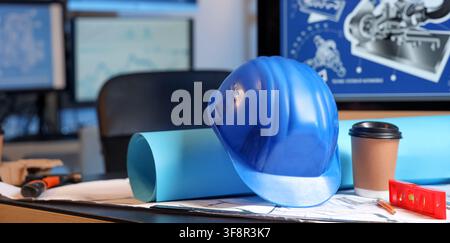 Blue hard hat and rolled blueprints on an architect's desk with Computer screens in a modern office setting, Computer screens displaying technical dra Stock Photo
