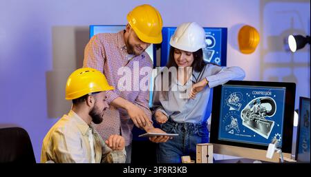 Engineering team collaborating on a digital tablet and computer screen with compressor blueprint design, the professionals wear hard hats Stock Photo