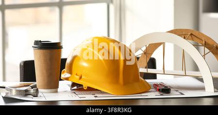 Yellow hard hat coffee cup and bridge model on blueprints architecture engineering and construction planning, this composition the fields of architect Stock Photo