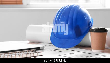 Blue hard hat, rolled blueprints, and coffee cup on architectural plans, construction industry and engineering design Stock Photo