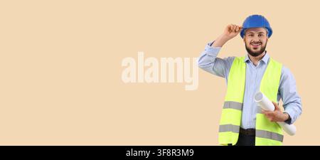 Smiling young male engineer in a blue hard hat and safety vest holding rolled blueprints, construction and architecture professional Stock Photo