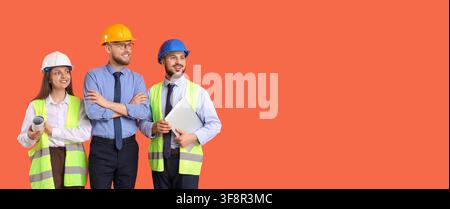 Three smiling construction workers and engineers wearing hard hats and safety vests, isolated on an orange background Stock Photo