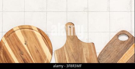 Three wooden cutting boards with natural grain patterns on a white tiled kitchen counter, top view with copy space Stock Photo