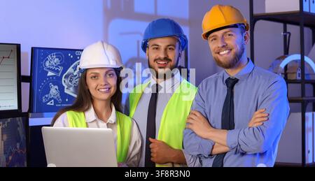 Smiling team of engineers and architects wearing hard hats and safety vests in a modern office with blueprints, They represent collaboration and teamw Stock Photo