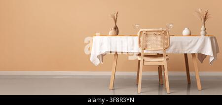 Minimalist dining room interior with a wooden table, white tablecloth, and rattan chair against a peach wall Stock Photo