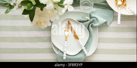 Elegant table setting with white plates, gold cutlery, and a mint green napkin on a striped tablecloth for a special occasion Stock Photo