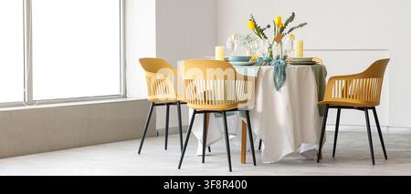 Modern dining room interior with yellow chairs and a table set with flowers and candles by a large window, the bright space is illuminated by natural Stock Photo
