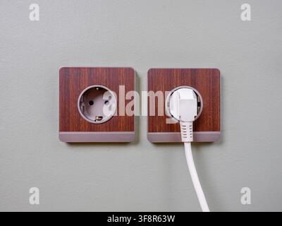 Two type F socket outlets mounted on pale green wall side-by-side. A white power plug is connected to the right socket. Stock Photo