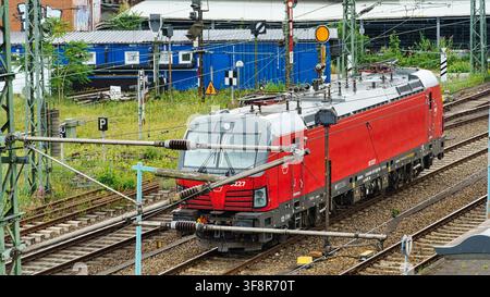 Hamburg, Germany - 22 July 2026: View of a red Siemens Vectron electric locomotive traveling on railway tracks in a rail yard, with overhead power lin Stock Photo