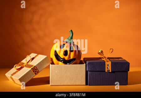 Jack o lantern emerging from gift box between wrapped presents on orange background for Halloween sale or party advertising Stock Photo