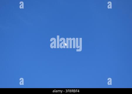 Half moon visible in clear bright blue daytime sky Stock Photo