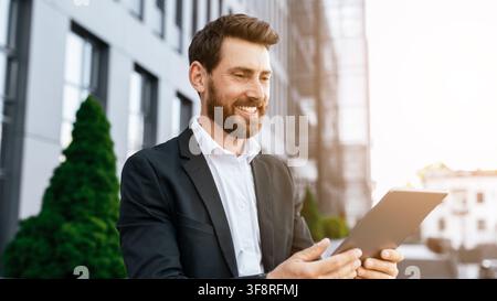 Smiling Caucasian Man Using Tablet Outdoors In Urban Setting, Business Concept Stock Photo