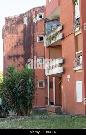 a stationary red brick building with balconies and plants in an urban residential area, captured from a ground level, slightly angled upward viewpoint Stock Photo