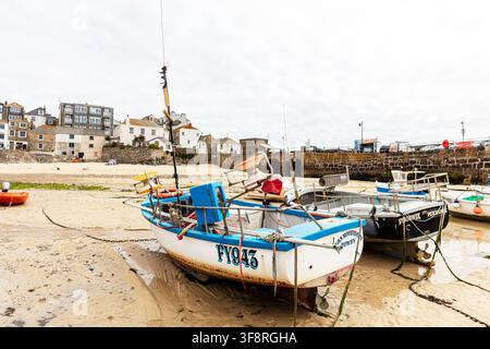 A low‑tide harbour scene at St Ives in Cornwall, showing several small fishing boats resting on the sandy seabed with ropes, buoys and seaweed scatter Stock Photo