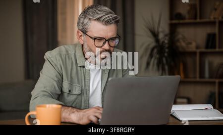 Focused Mature Man Working On Laptop In Modern Home Office, Business Concept Stock Photo