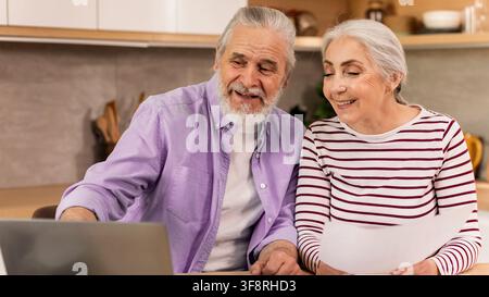 Happy Elderly Caucasian Couple Using Laptop Together At Home, Smiling, Loving Moment Stock Photo