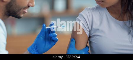 Healthcare Worker Administering Vaccine To Young Black Female Patient In Clinic, Healthcare Concept Stock Photo