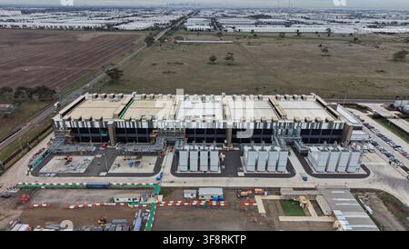 Large data center building under construction with cooling units and parking, surrounded by industrial area and farmland Stock Photo