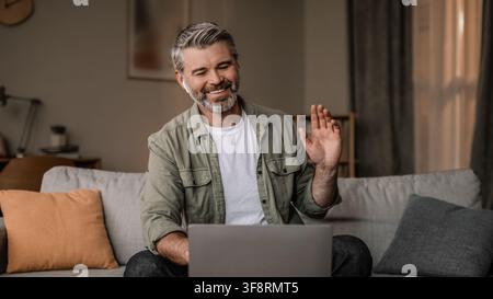 Happy Caucasian Man Waving While Using Laptop At Home, Remote Work Concept Stock Photo