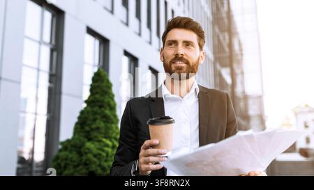 Confident Businessman Holding Coffee And Blueprints, Smiling Outside Modern Office, Business Concept Stock Photo