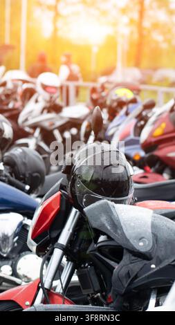 Close up view of black full face motorcycle helmet covered in raindrops, resting on red motorcycle. Strong sun flare effect background, blurred array Stock Photo