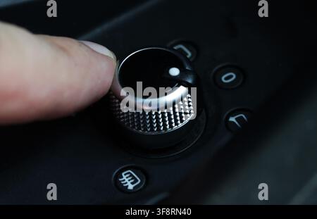 Close up perspective of human finger rotating textured metallic knob, part of car interior control system for mirror adjustment or ventilation, showin Stock Photo