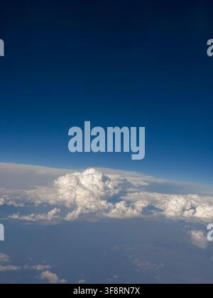 Aerial view of dramatic white cumulus clouds beneath a deep blue sky, photographed through an airplane window at high altitude Stock Photo