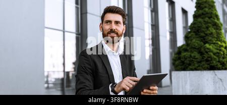 Confident Caucasian Male Businessman Using Tablet Outside Modern Office Building, Business Concept Stock Photo