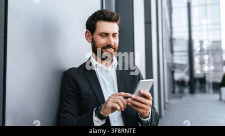 Businessman Smiling While Using Smartphone In Modern Office, Digital Communication Concept Stock Photo