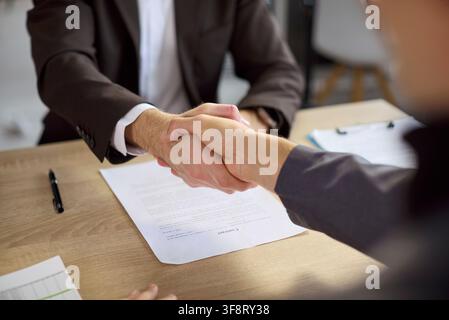 Executives shaking hands over contract documents to finalize a business deal Stock Photo