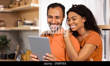 Happy Multiracial Couple Smiling Together While Using Tablet At Home, Relaxed Lifestyle Stock Photo