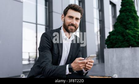 Smiling Caucasian Male Businessman Using Smartphone At Modern Office, Business Concept Stock Photo