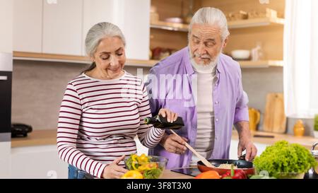 Happy Elderly Caucasian Man And Woman Cooking Together In Kitchen, Preparing Healthy Meal Stock Photo