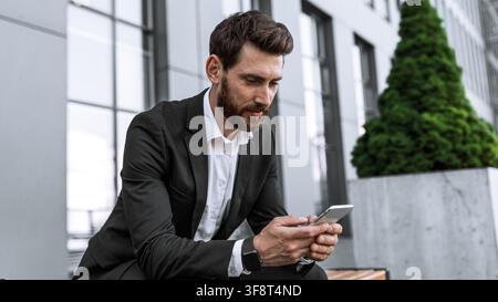 Businessman Using Smartphone Sitting Outdoors, Professional Adult Male In Suit, Business Concept Stock Photo