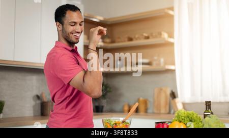 Happy Young African American Man Cooking Healthy Salad In Modern Kitchen, Nutrition Concept Stock Photo