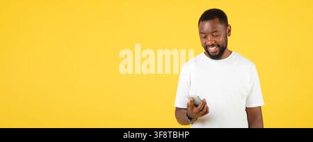 Smiling Black Man Using Smartphone On Yellow Background, Technology Concept Stock Photo