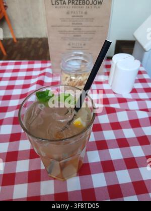 A cold refreshing summer drink or mojito cocktail with ice cubes and fresh mint leaves in a glass with a black straw on a red and white checkered tabl Stock Photo